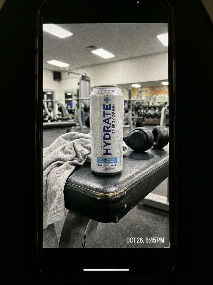 A phone photo of a can on a gym bench next to a towel and headphones