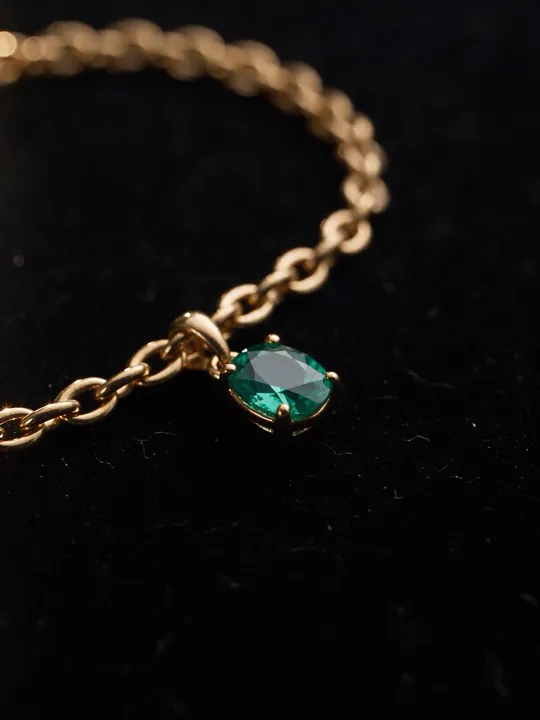 Macro of a gold chain bracelet with an emerald pendant on black velvet
